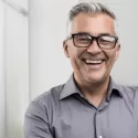 A confident middle-aged man with gray hair and glasses smiling after full-arch All-on-4 dental implant treatment at Chapel Hill Oral Surgery.