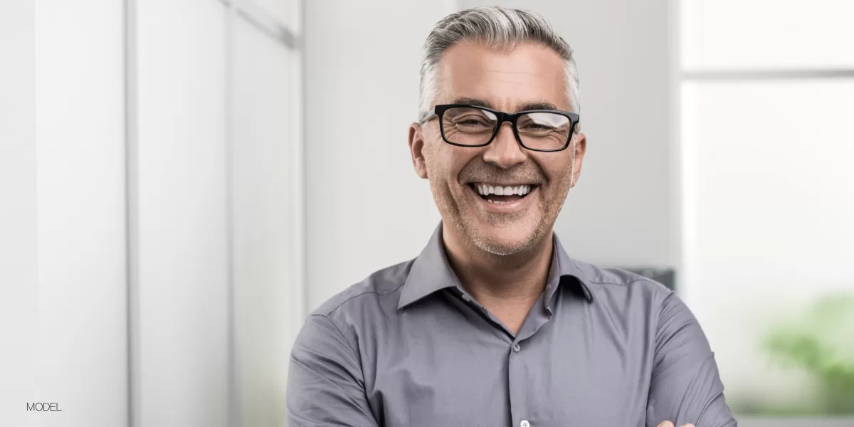 A confident middle-aged man with gray hair and glasses smiling after full-arch All-on-4 dental implant treatment at Chapel Hill Oral Surgery.