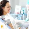 A patient sitting in a dental chair smiling and speaking with an oral surgeon during a consultation about anesthesia.