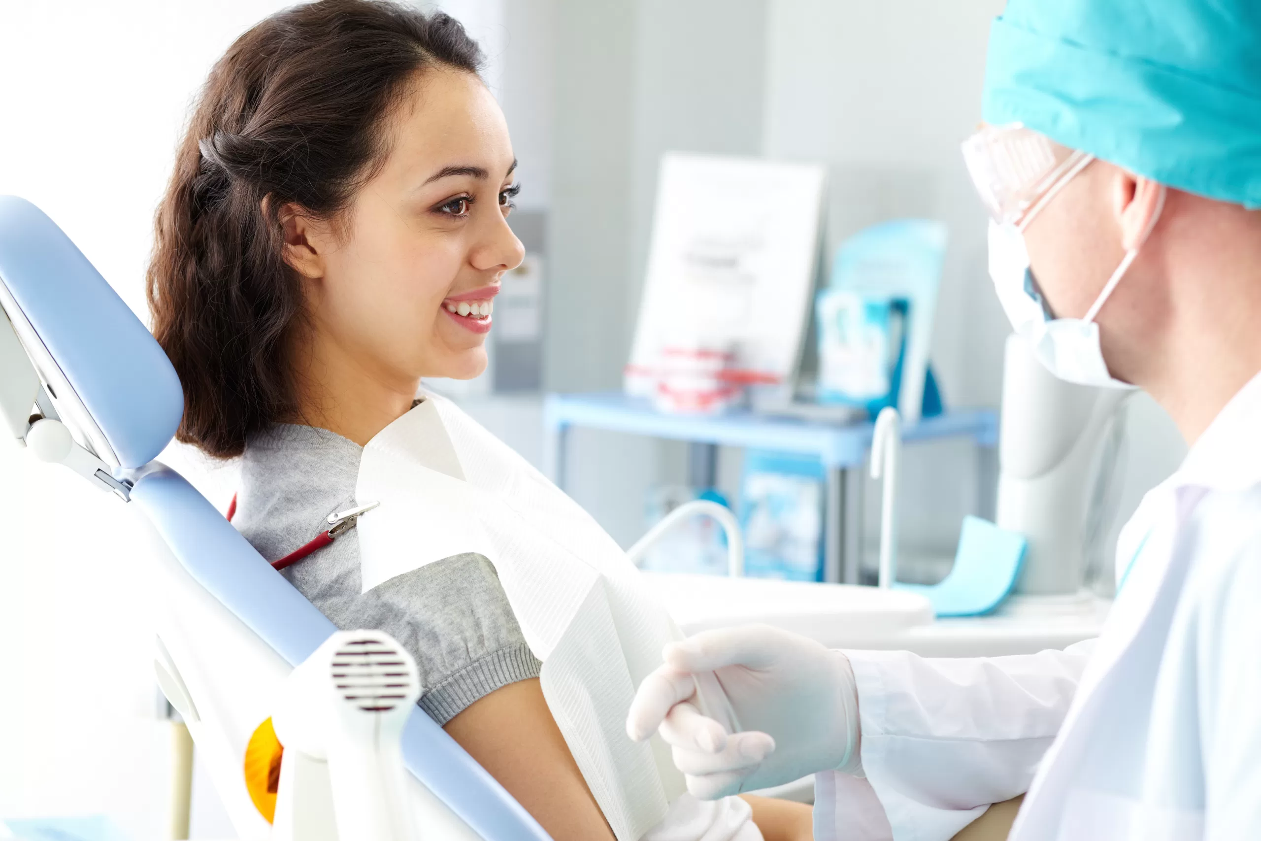A patient sitting in a dental chair smiling and speaking with an oral surgeon during a consultation about anesthesia.
